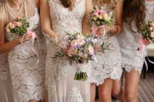 Bride and bridesmaids in white lace standing together with a pink bouquets.