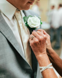 Groom is wearing a gray tuxedo and mother of the bride is pinning boutonniere. 